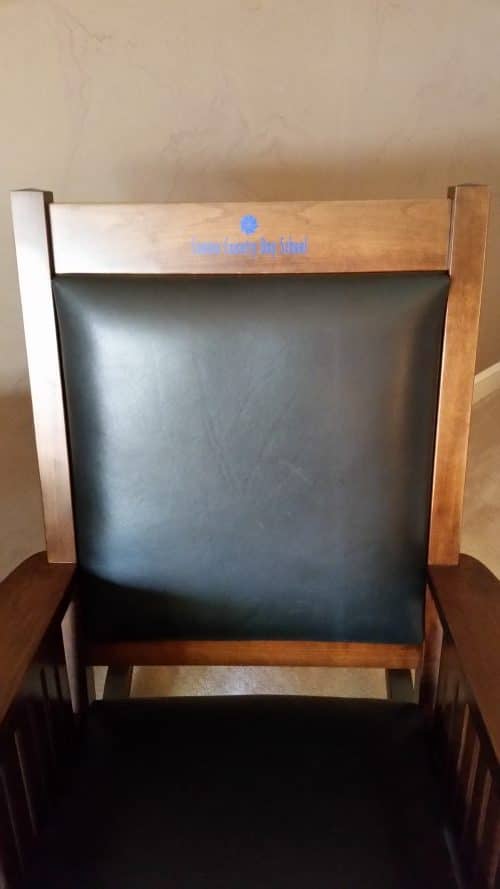 blue logo on brown amish rocking chair with black leather on brown chair