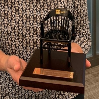 Employee of Fair Health in office holding black miniature college chair with brown maple base - miniature college chairs