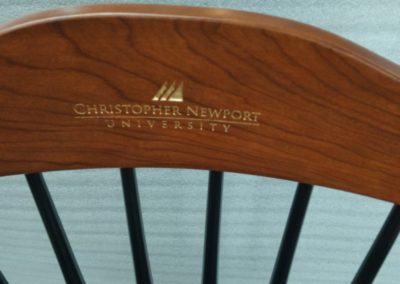Close-up view of the engraved logo of Christopher Newport lUniversity on a black Captain's chair with cherry crown and arms