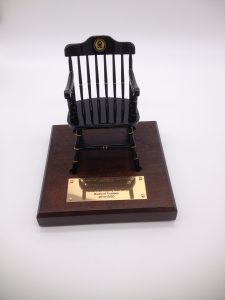 front view of black miniature captain's chair of LaJolla country Day School on brown base with brass plate