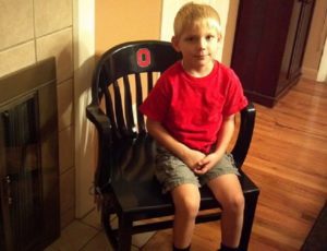 Young boy, Joey, sitting in his ACAC Chair of OSU with Block 'O' logo